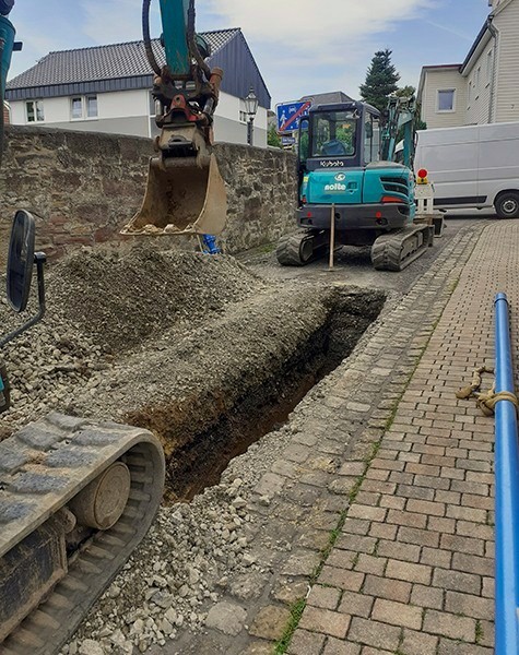 Bagger hebt Kanalgraben mit neuer blauer Wasserleitung in gepflasterter Altstadtgasse in Hofgeismar aus