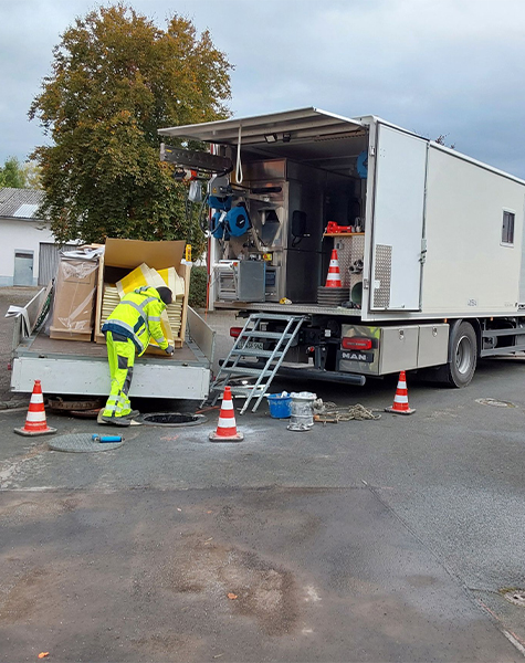 Mitarbeiter bei Kanalsanierungsarbeiten an einem Schacht neben einem mobilen Sanierungsfahrzeug.
