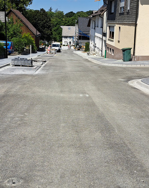 Neu asphaltierte Straße mit Gehwegen und laufenden Bauarbeiten in einem Wohngebiet.